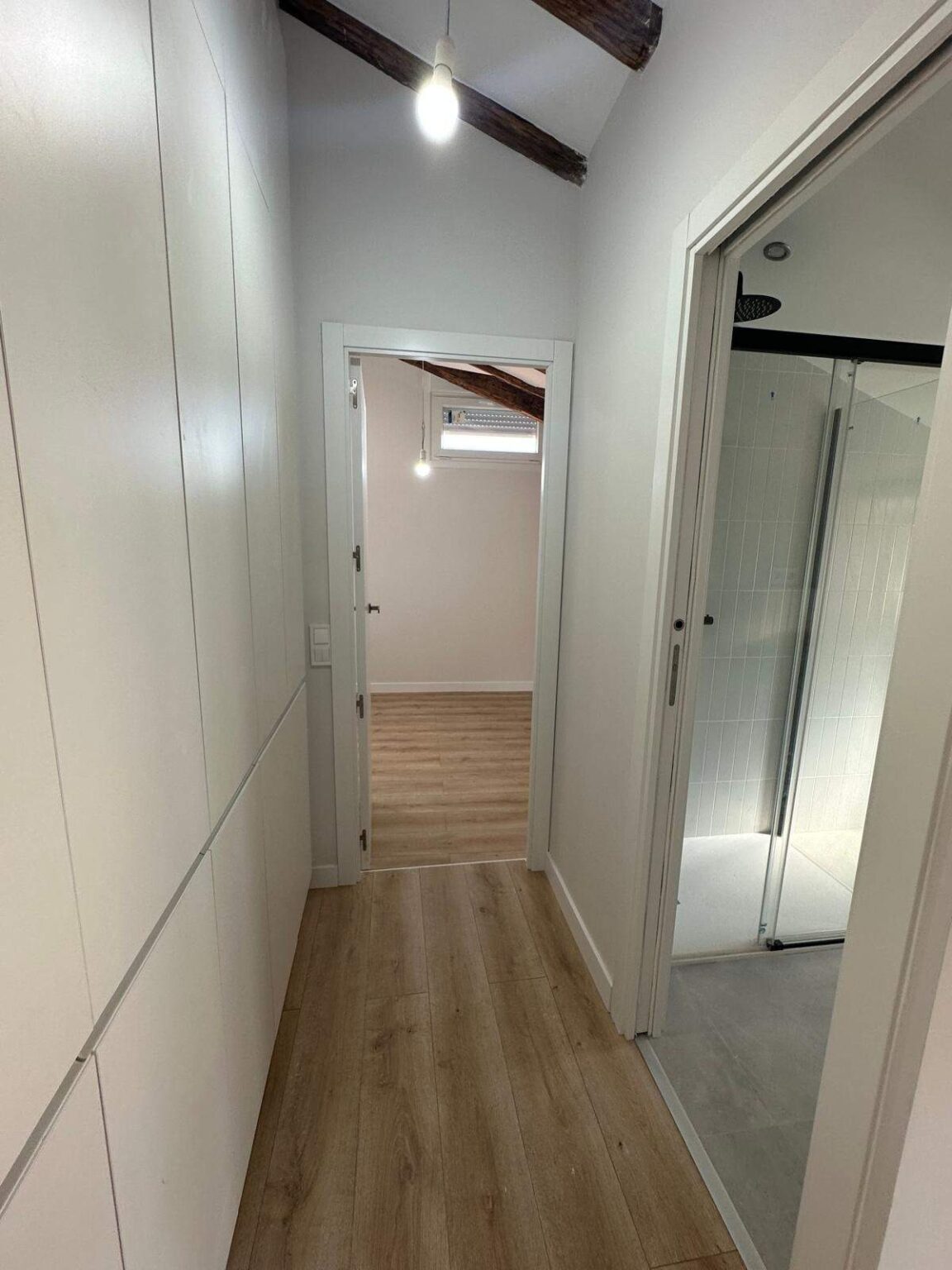 Pasillo de vivienda con suelo de madera y paredes blancas en reforma integral en Madrid