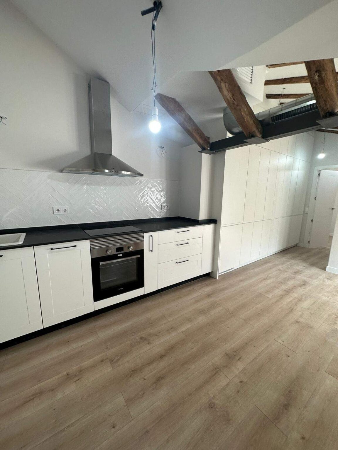 Cocina blanca con campana extractora y suelo de madera en reforma integral de vivienda