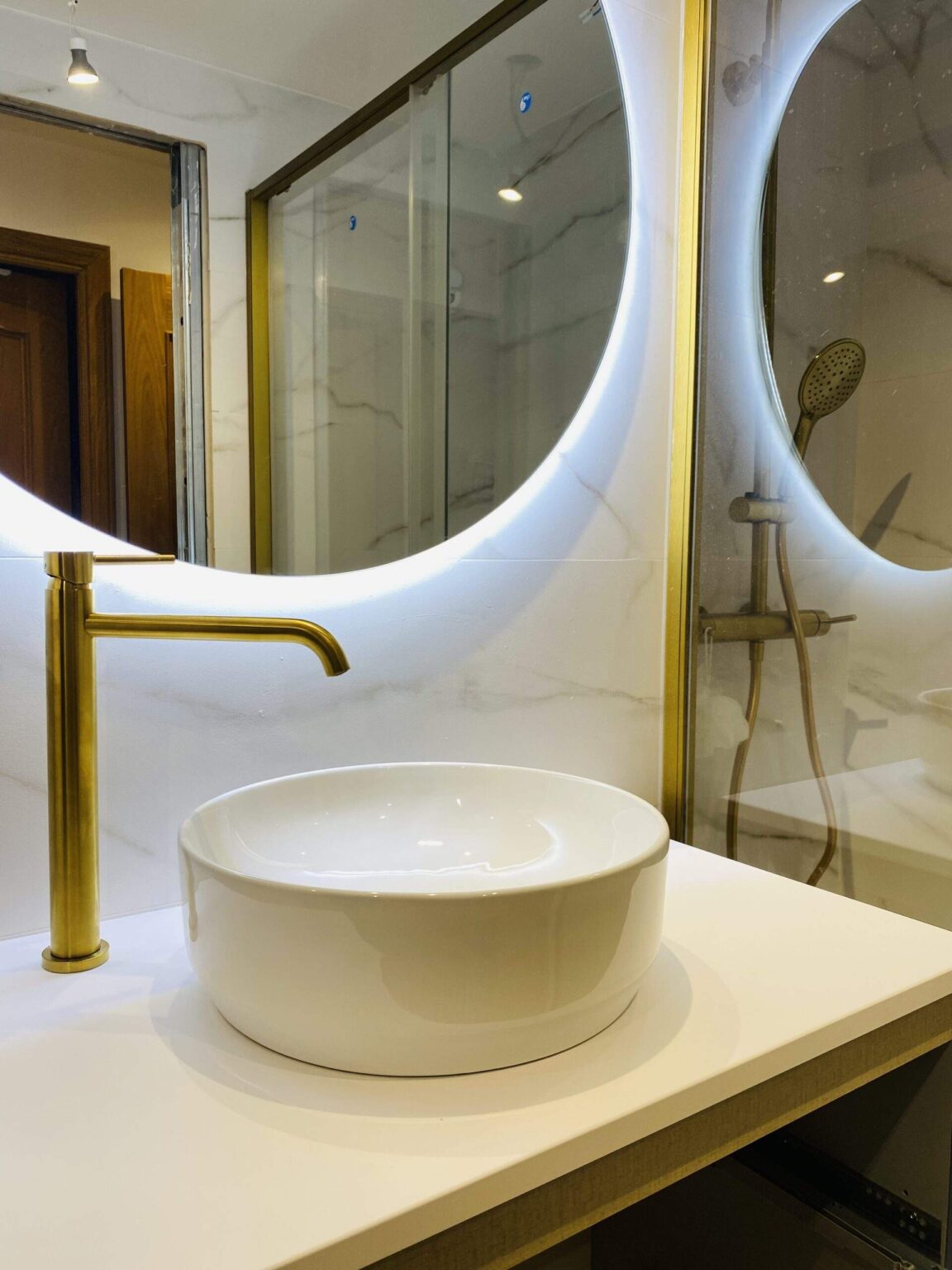 Baño moderno con lavabo redondo y grifería dorada en reforma de interiorismo en Madrid