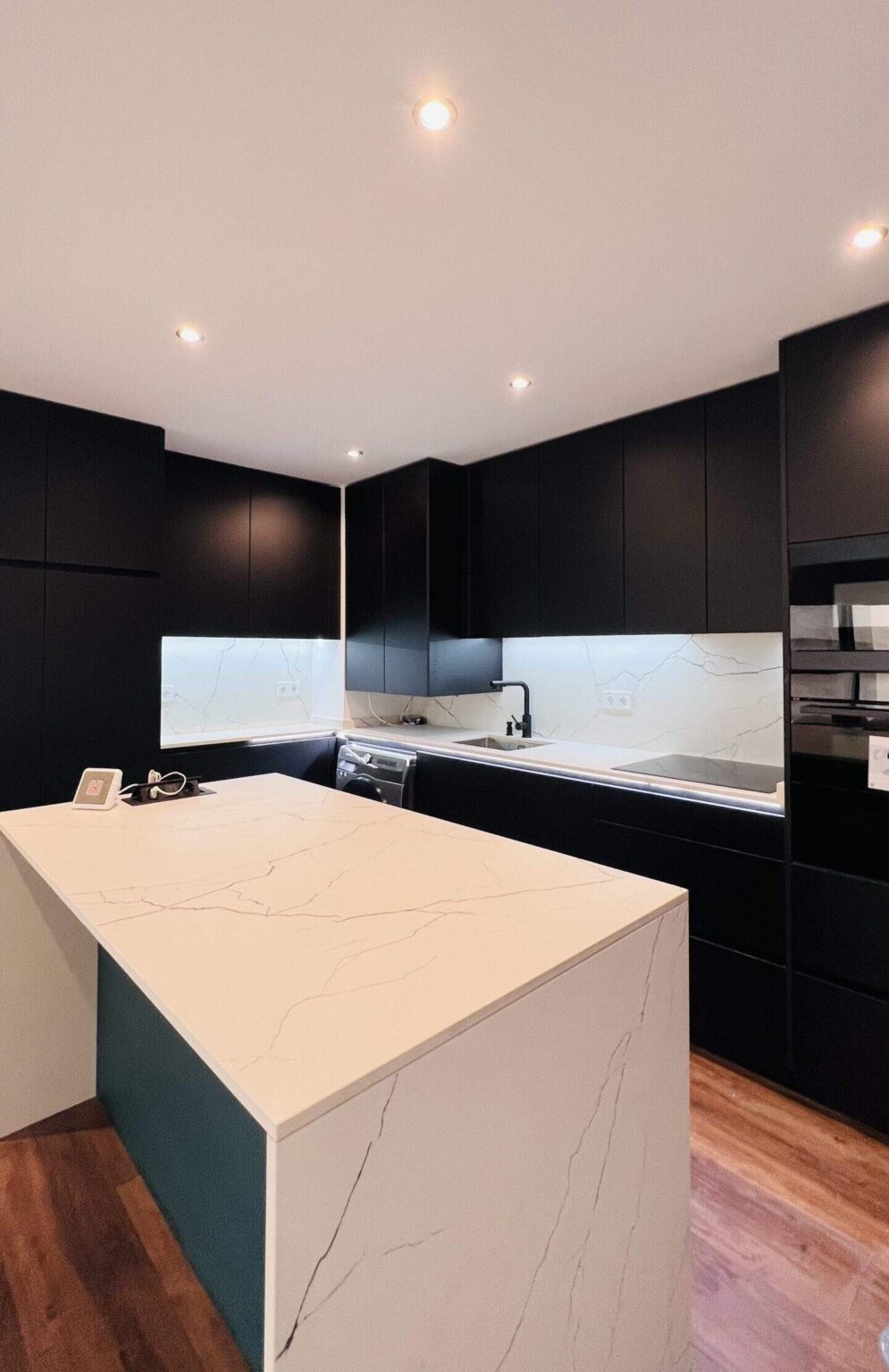 Cocina negra con isla central y encimera blanca en reforma integral de vivienda en Madrid