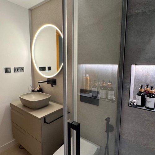 Baño moderno con espejo retroiluminado y lavabo suspendido en proyecto de interiorismo